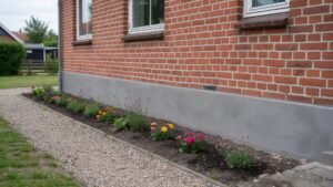 Nypudset grå sokkel på rødt murstenshus med blomsterbed